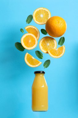 Tasty ripe oranges and green leaves over glass bottle on light blue background clipart