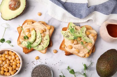 Humuslu lezzetli sandviçler ve beyaz mermer masada malzemeler.