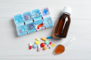 Bir şişe şurup, ilaç kaşığı ve beyaz ahşap masa üzerinde haplar, düz yatak. Grip ilacı.