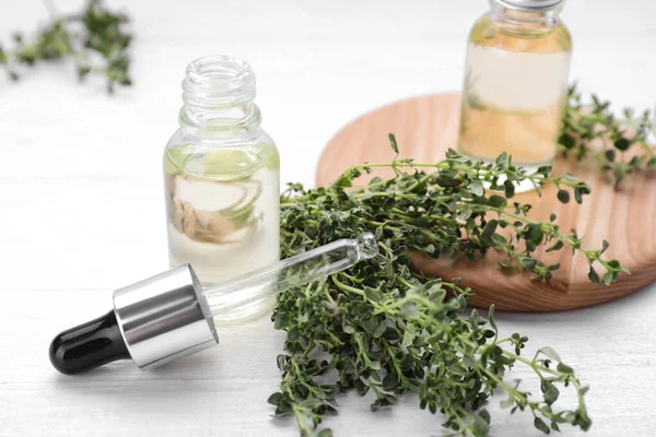 Thyme essential oil and fresh plant on white wooden table