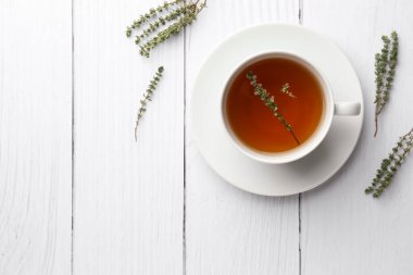 Beyaz ahşap masa üzerinde kekik olan bir fincan aromatik bitki çayı. Metin için boşluk