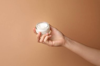 Bej arka planda bir kavanoz yüz kremi tutan kadın, yakın plan. Metin için boşluk