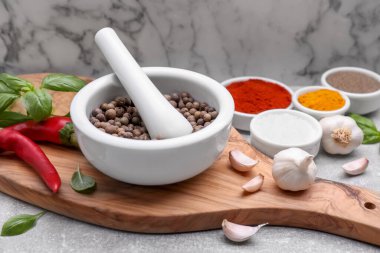 Topuzlu havan topu ve beyaz mermer duvara karşı açık gri masada farklı baharatlar.