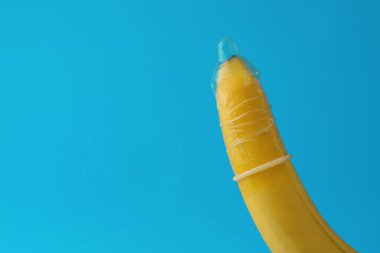 Açık mavi arka planda prezervatifli muz, yakın plan ve metin için yer. Güvenli seks konsepti