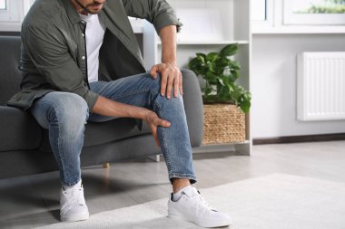 Evdeki kanepede bacağında ağrıdan muzdarip bir adam, yakın plan. Metin için boşluk