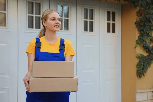 Courier in uniform with parcels near private house outdoors, space for text