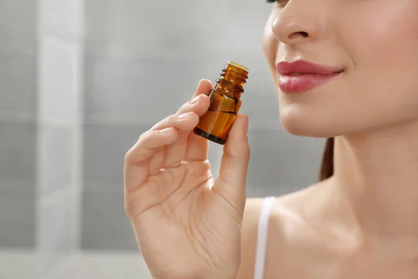 Young woman smelling essential oil indoors, closeup