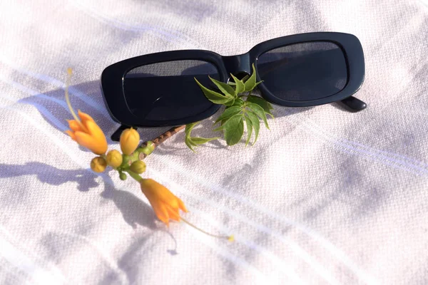 Stylish sunglasses and tropical flower on blanket, closeup