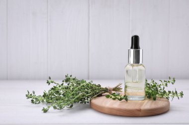 Bir şişe kekik yağı ve beyaz ahşap masada taze bitki, metin için yer var.