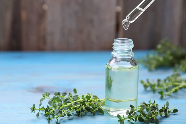Thyme essential oil dripping from pipette into bottle on light blue wooden table, space for text