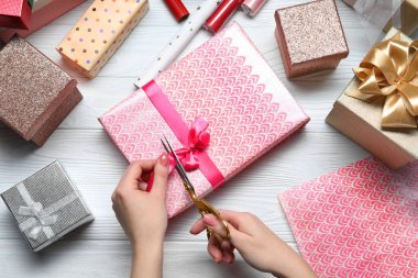 Beyaz ahşap masada hediye kutusu dekore eden kadın, üst manzara.