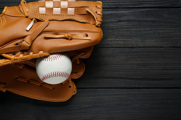 Catcher\'s mitt and baseball ball on black wooden table, top view with space for text. Sports game