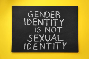 Blackboard with text Gender Identity Is Not Sexual Identity on yellow background, top view clipart