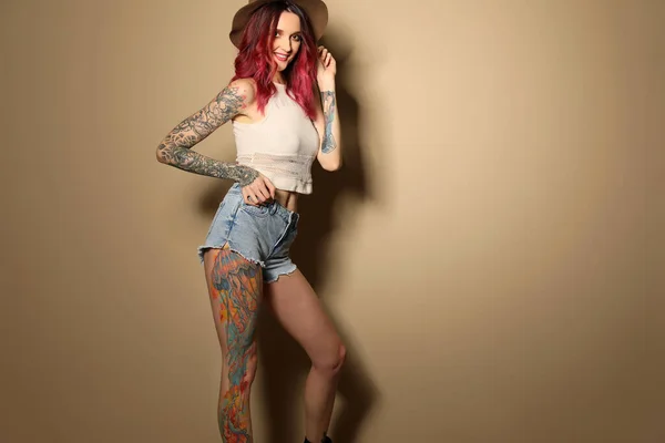 Beautiful woman with tattoos on body against beige background