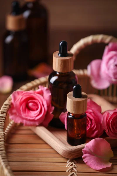 Bottles of essential rose oil and flowers on tray