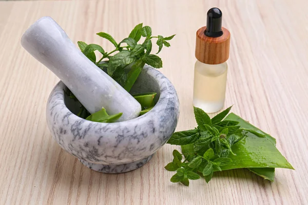 Mortar with pestle, herbs and bottle of essential oil on wooden table