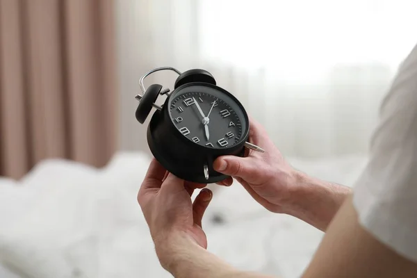 Man with alarm clock in bedroom, closeup of hands
