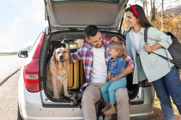 stock image Parents, their daughter and dog sitting in car trunk outdoors. Family traveling with pet