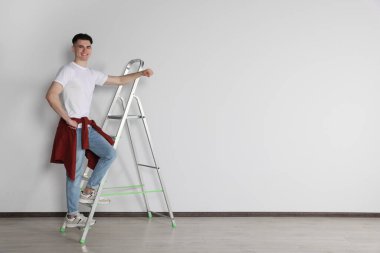 Kapalı alandaki beyaz duvarın yanında merdivene tırmanan tamirci. Metin için boşluk