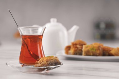 Bir bardak geleneksel Türk çayı ve beyaz masada lezzetli baklava, metin için yer