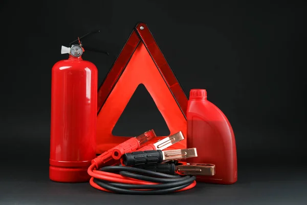 Emergency warning triangle, red fire extinguisher, battery jumper cables and motor oil on black background. Car safety