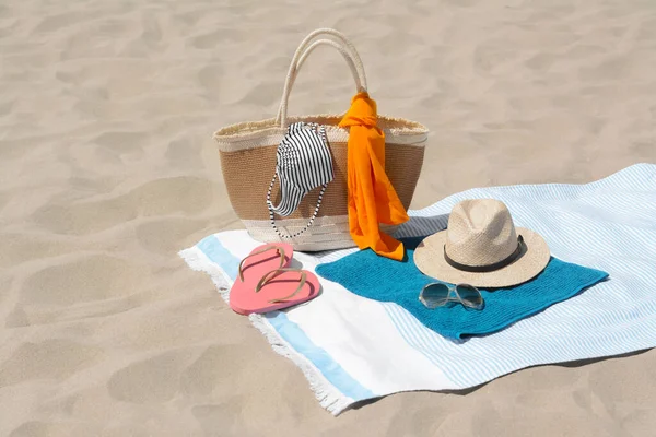 Blue blanket with towel, bag and beach accessories on sand