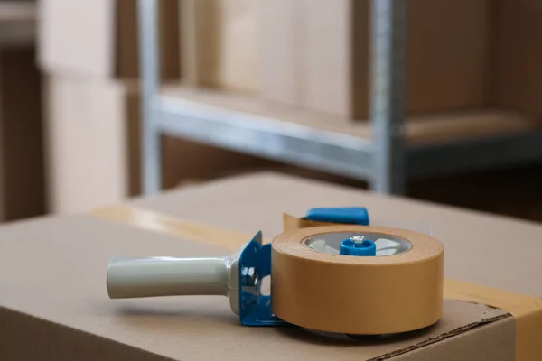 Adhesive tape dispenser on cardboard box indoors. Space for text