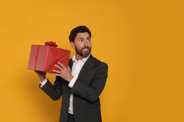 Stock image Emotional man holding gift box on yellow background, space for text