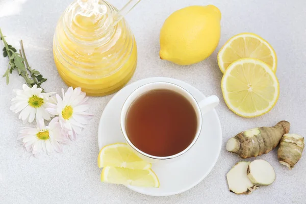 Cup of delicious tea with honey, lemon and ginger on white table, above view