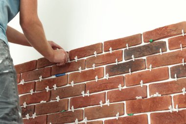 Profesyonel müteahhit duvara dekoratif tuğla yapıştırıyor, yakın plan. Döşeme kurulum süreci