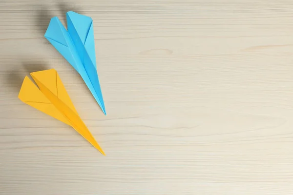 Handmade paper planes in light blue and yellow colors on beige wooden table, flat lay. Space for text
