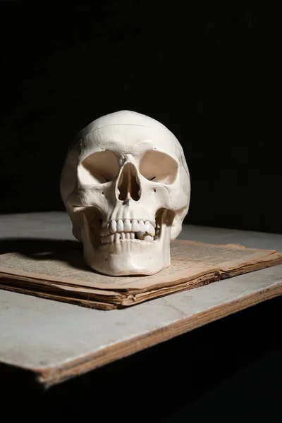 Human skull and old book on table against black background