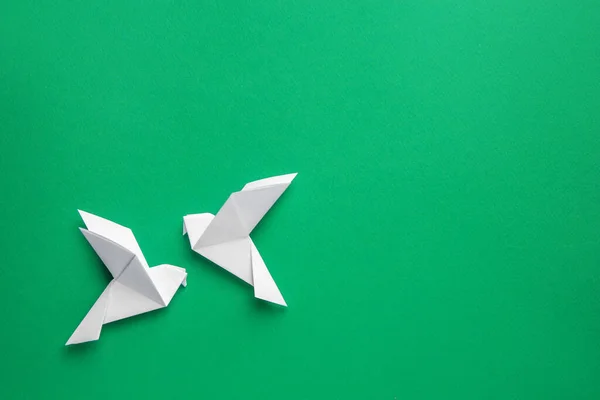Beautiful white origami birds on green background, flat lay. Space for text