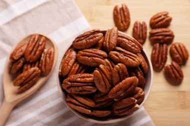 Tasty pecan nuts with bowl, spoon and cloth on wooden table, flat lay clipart