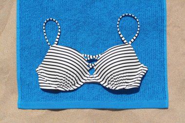 Blue beach towel and swimsuit on sand, top view