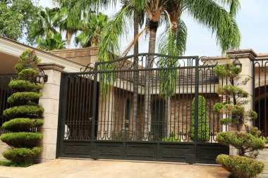 Bina ve palmiye ağaçları yakınında siyah metal kapılar