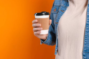 Turuncu arka planda içkisi olan bir kadın, yakın çekim görüntüsü ve mesaj için yer tutuyor. Kahve hazır.