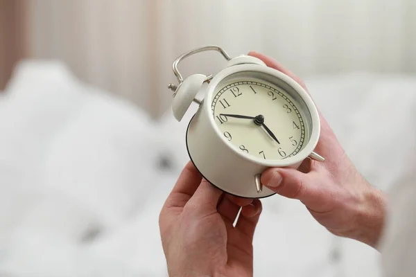 Man with alarm clock in bedroom, closeup of hands. Space for text