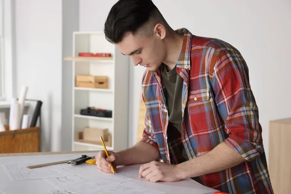 Young handyman working with blueprints at table in room