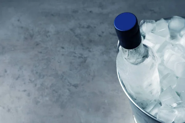 Bottle of vodka in metal bucket with ice on grey table, above view. Space for text