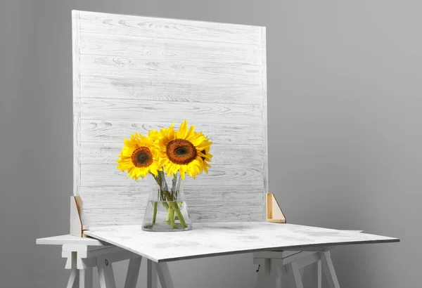 Glass vase with beautiful sunflowers and double-sided backdrop on table in photo studio