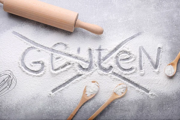 Crossed out word Gluten and different kitchen utensils on grey background, flat lay