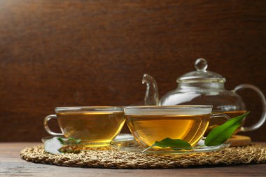 Cam bardaklarda taze yeşil çay, ahşap masada yapraklar ve çaydanlık.