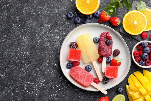Plate of different fruit ice pops on black textured table, flat lay. Space for text