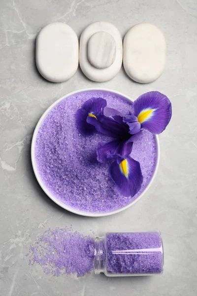 Plate and jar with purple sea salt, spa stones, beautiful flower on grey marble table, flat lay