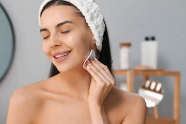 Young woman using cotton pad with micellar water indoors