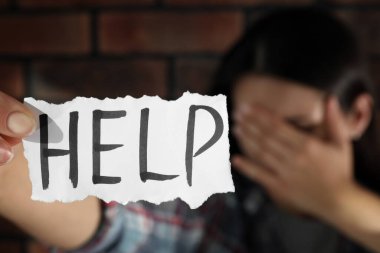 Aile içi şiddet kavramı. Elinde yazılı kağıt olan mutsuz kadın tuğla duvarın yanında dur, eline odaklan.