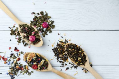 Düz kompozisyon, kaşık kaşık kurutulmuş bitki çayı yaprakları ve beyaz ahşap masada meyveler. Metin için boşluk