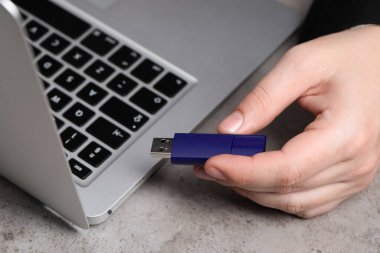 USB bellekli bir adam gri masada dizüstü bilgisayarın yanında, yakın plan.