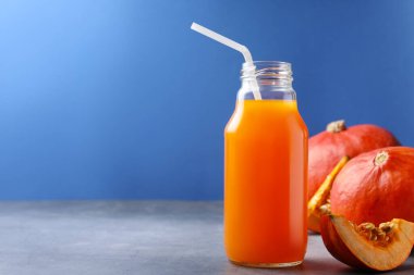 Cam şişede bal kabağı suyu ve açık gri masada mavi arka planda balkabağı. Metin için boşluk